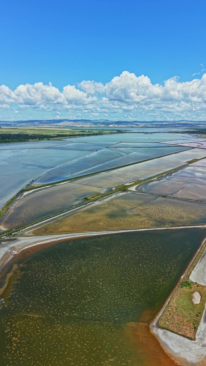 Vue large de marais salants et de plans d'eau dans une zone côtière sous un ciel bleu.