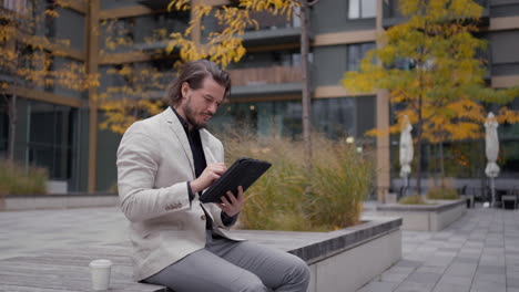 Serious-businessman-in-formal-wear-working-on-pad-at-city-street