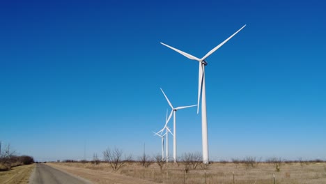 wind turbines slowly spinning in a field near a road