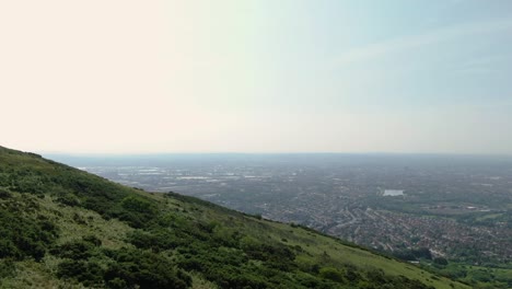 drone flight over green mountain towards city with haze on the horizon