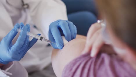 caucasian woman and female doctor wearing face masks, vaccinating