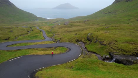 solo woman walks along scenic winding road of nordradalsskard, faroe islands