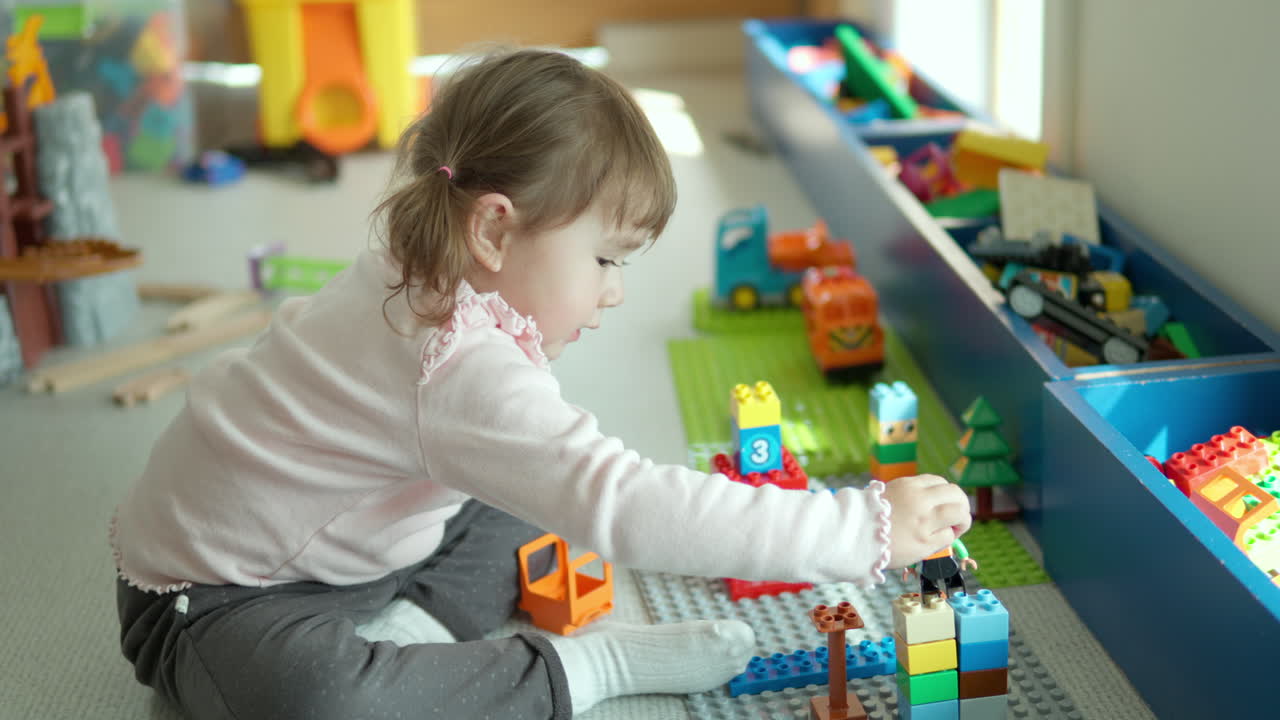 niña rubia juguetona de 3 años jugando con bloques de lego en la sala de juegos de casa