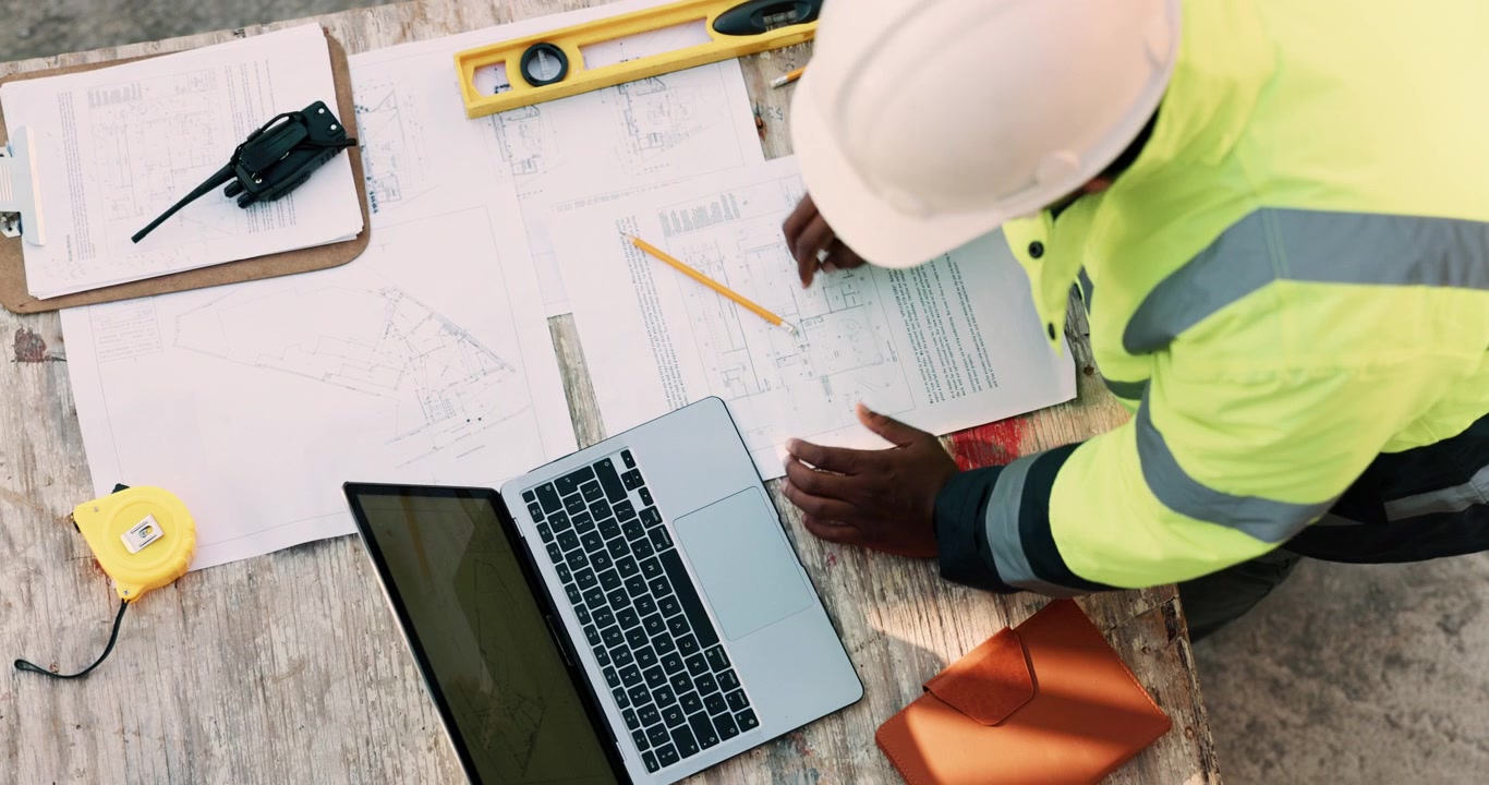Construction Engineer Working on Blueprints and Laptop at Site