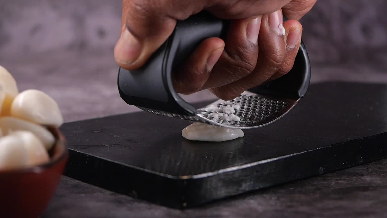 Mano che schiaccia uno spicchio d'aglio con uno spremiaglio