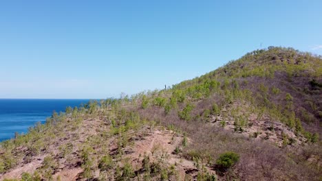 Paisaje-Aéreo-De-La-Estatua-De-Cristo-Rei-Jesucristo-Descendiendo-Sobre-Montañas-Y-Colinas-Escarpadas-Con-Vistas-Al-Océano-Azul-En-Dili,-Timor-leste