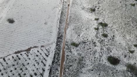 Draufsicht-Der-Drohne,-Die-Dem-Fahrzeug-Auf-Einer-Unbefestigten-Straße-Nach-Einem-Schneesturm-Und-Weinbergen-Folgt,-Israel