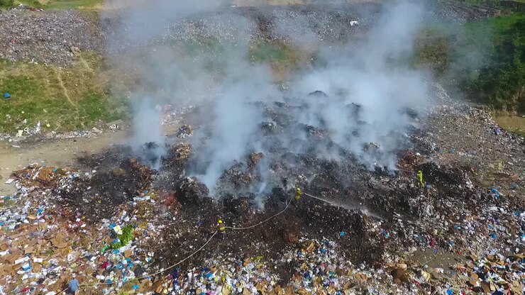 Aerial view around Firefighters calming a burning junkyard- circling, drone shot