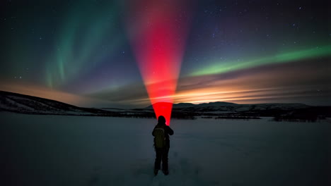person with red light beam under dazzling northern lights in a snowy winter landscape