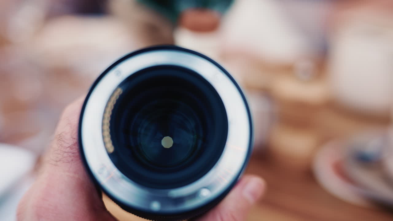 Primo piano dell'obiettivo di una fotocamera tenuto in mano con un effetto bokeh sullo sfondo.