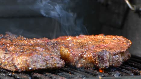 un jugoso filete de costilla sentado en una parrilla con una pequeña llama naranja junto a la carne cocinada a cámara lenta