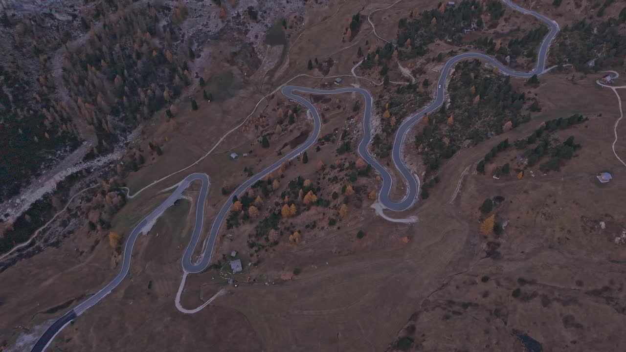Gardena Pass road winds through Dolomites at sunrise, drone perspective
