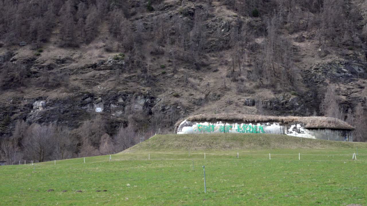 Concrete Bunker with Graffiti on a Grassy Hillside with Bare Trees