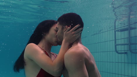 Pareja-Joven-Besándose-Bajo-El-Agua-En-La-Piscina-Disfrutando-De-Un-Beso-íntimo-Amantes-Románticos-Sumergidos-En-Agua-Flotando-Con-Burbujas-En-Una-Intimidad-Apasionada