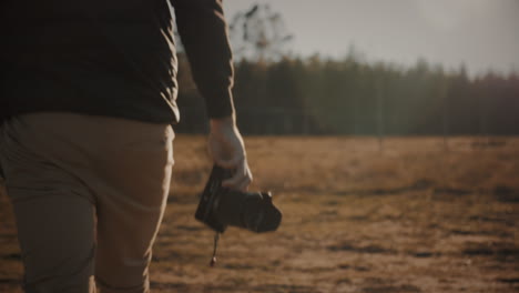 photographer walks holding a camera in his hand at sunset or sunrise