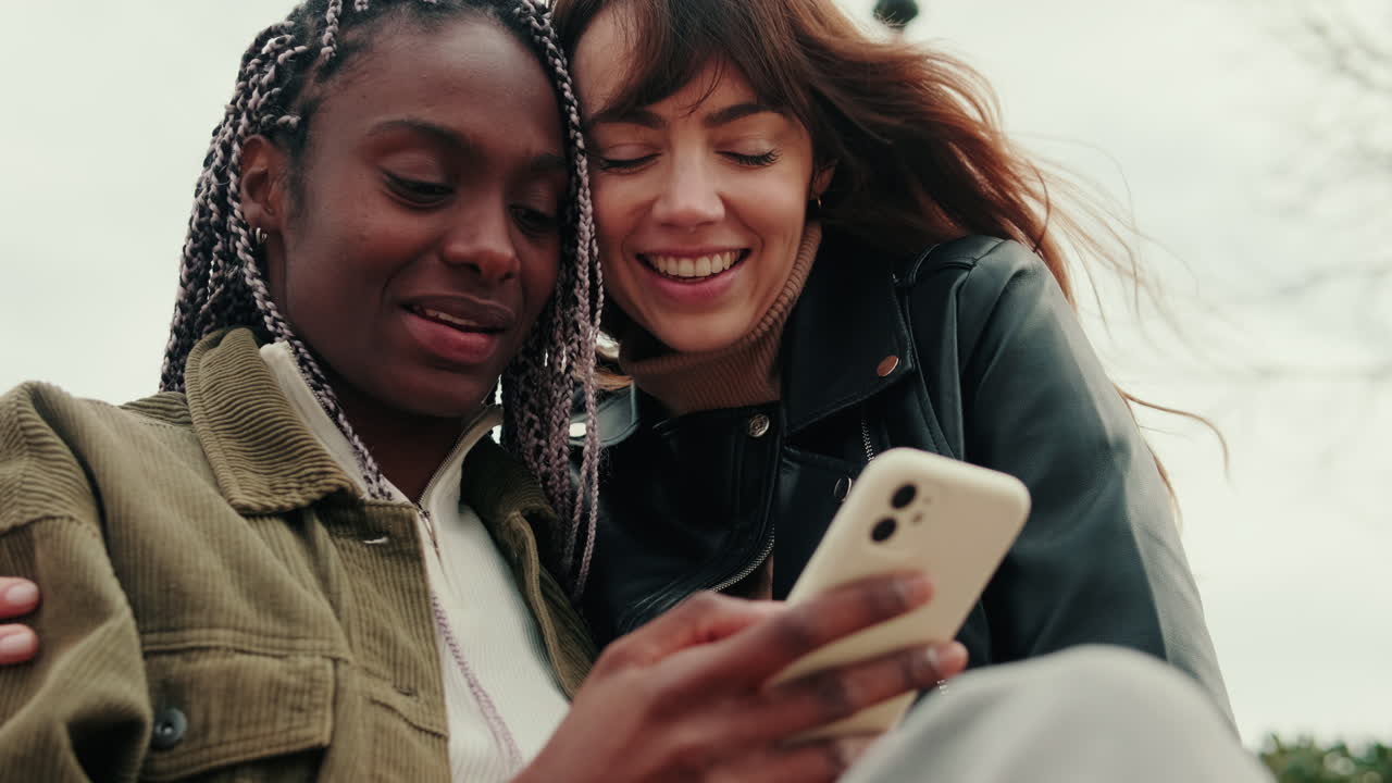 Due giovani donne che si abbracciano e guardano lo smartphone all'aperto