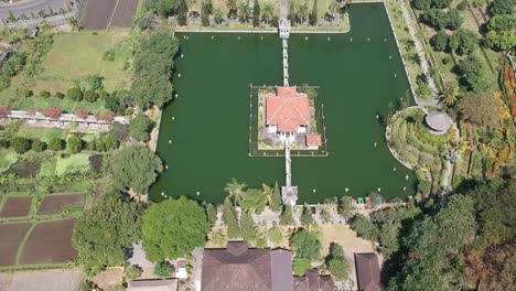 aerial pan up view from field to reveal building surrounded by moat in bali, indonesia