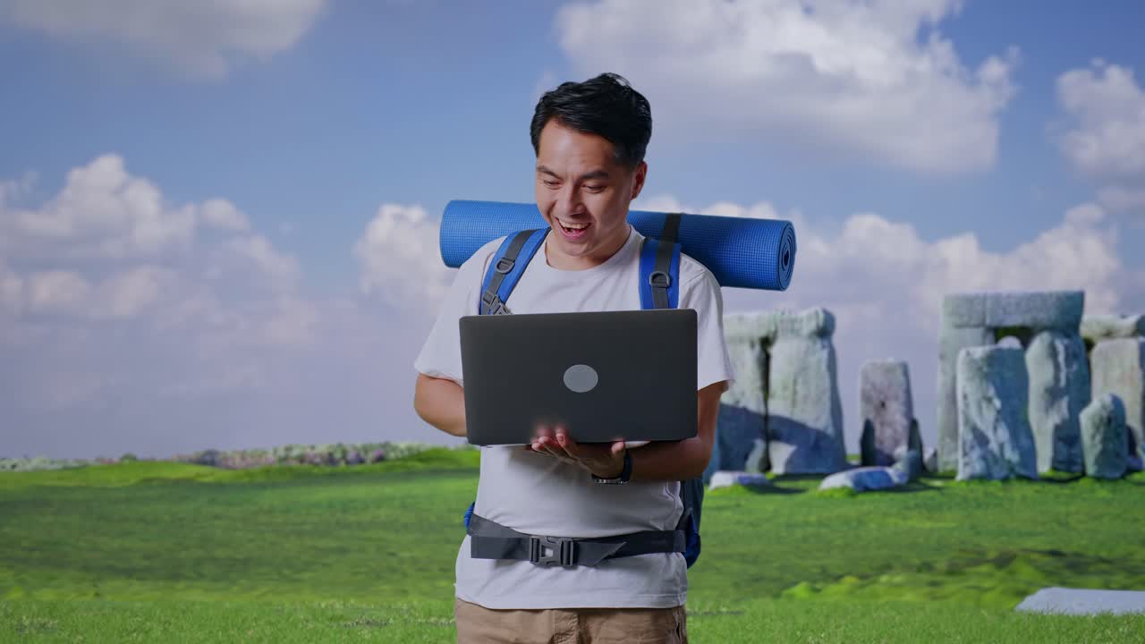 Aziatische mannelijke wandelaar met bergbeklimmersrugzak kijkt naar een laptop en zegt 'wow' tijdens het reizen in Stonehenge