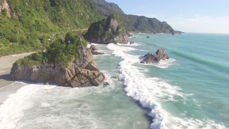 a beautiful and stunning landscape in the west coast of new zealand with ocean waves splashing at the shore surrounded by green mountains- wide shot