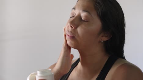 una mujer latina adulta aplica un tratamiento de hidratación natural a su cara.