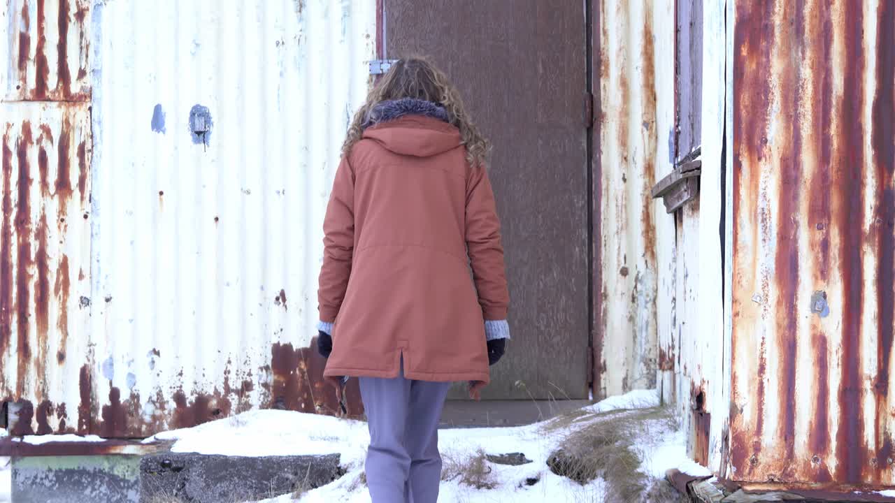The camera moves from down to up, slowly unveiling a girl going to the ruins of a damaged farm.