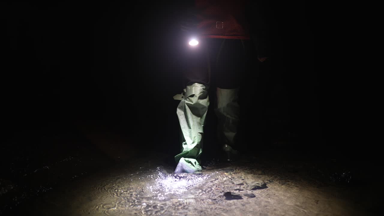 persona caminando en un río por la noche con una linterna