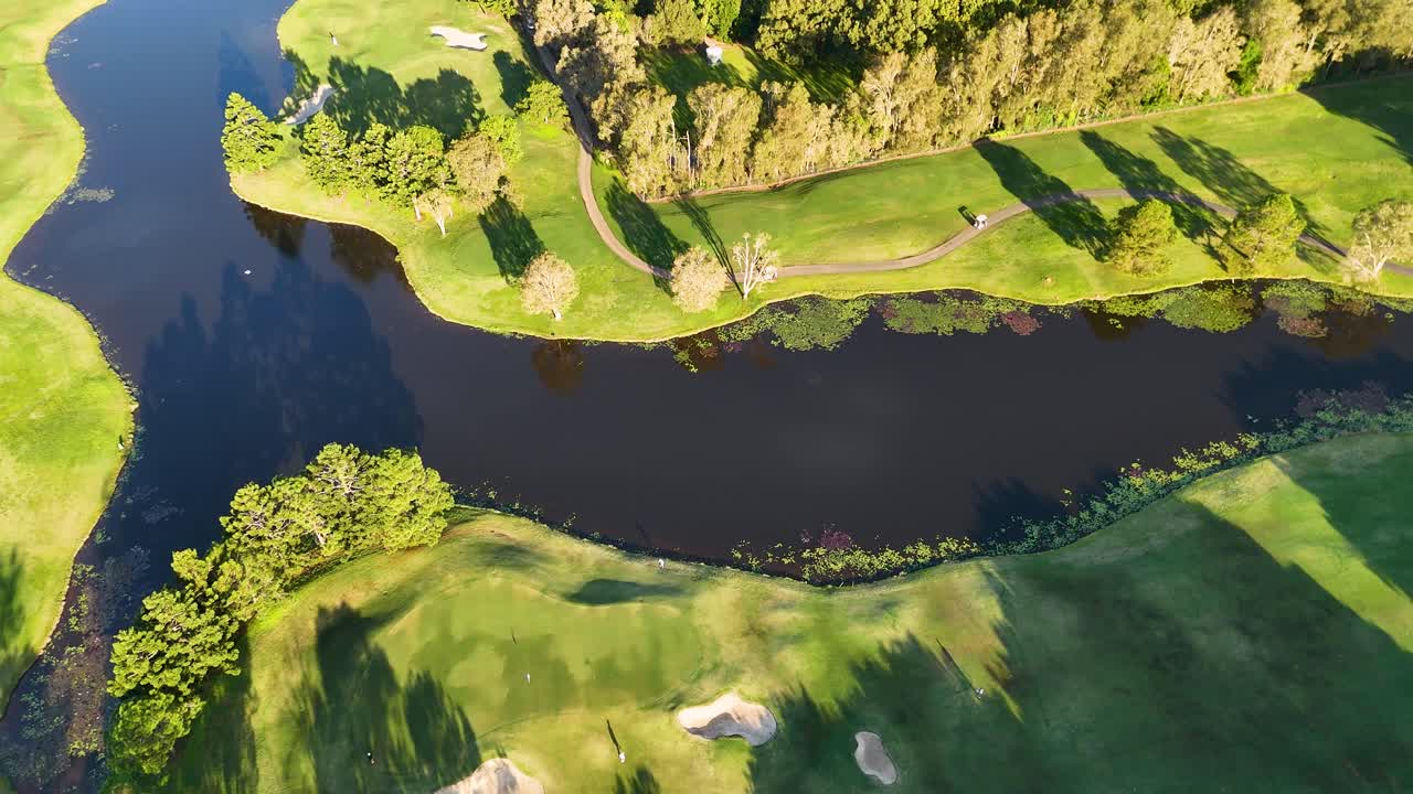 Drone footage captures a lush golf course with water hazards and vibrant greenery under bright sunlight