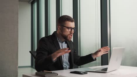 A-man-in-business-clothes-scolds-an-employee-over-a-video-call-while-sitting-at-a-laptop