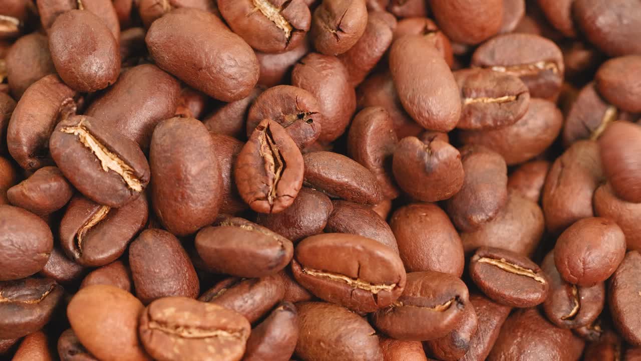 Close-up video of roasted coffee beans tumbling, highlighting texture and rich brown tones under soft lighting