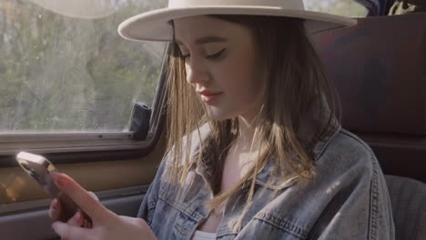 Una-Hermosa-Joven-Escribiendo-En-Su-Teléfono-Celular-Mientras-Sonríe-Durante-Un-Viaje-Por-Carretera-En-La-Caravana