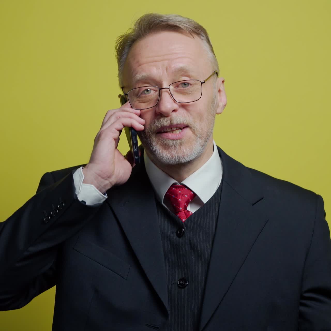 Ritratto di anziano uomo d'affari sorridente che parla al cellulare. Uomo maturo allegro in costume che parla al telefono cellulare su sfondo giallo