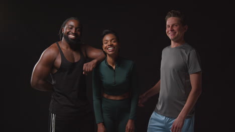 studio portrait of group of smiling male and female athletes in fitness clothing training shot against black background