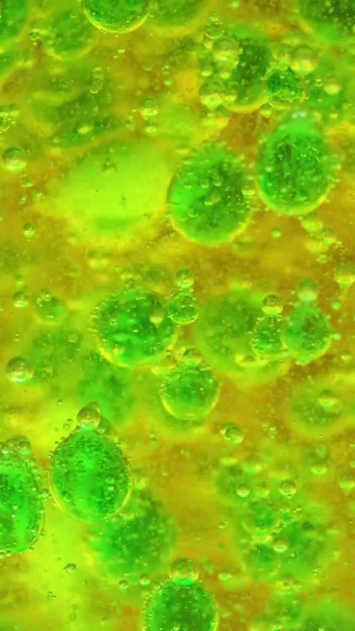 Visão macro de bolhas efervescentes verdes vibrantes reagindo e flutuando em um fluido amarelo.