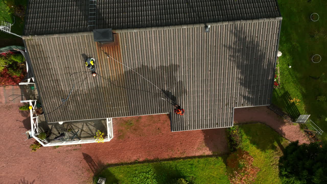 Ripresa aerea dall'alto con drone che ruota sopra una donna che lava il tetto di una casa, giornata autunnale