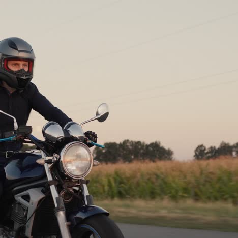 A-young-biker-in-black-clothes-rides-along-the-fields-of-corn