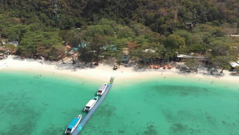 banana beach pier across shallow emerald sea with tourists tour boats in koh hey , thailand - aerial tilt-down fly-over rotation shot