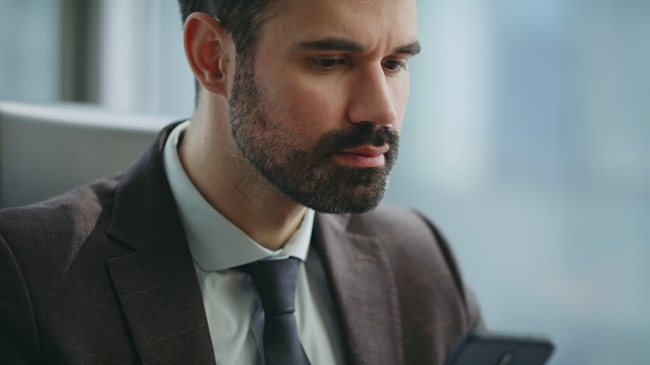 Imprenditore che invia messaggi dal cellulare, seduto in ufficio, primo piano. Manager che usa il telefono.