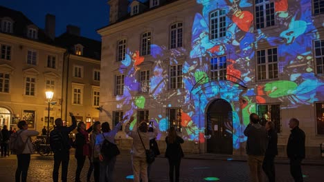captivating nighttime spectacle: a colorful projection show illuminating a historic building while an enchanted audience engages with the mesmerizing visual display