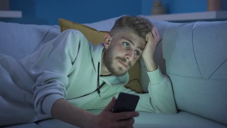 handsome young man using phone at home in a sad and depressed mood.