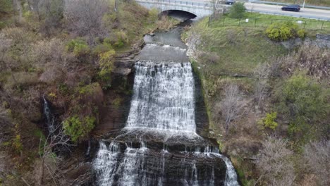 aerial ascending ribbon waterfall on niagara escarpment with cars crossing road, devil's punch bowl hamilton