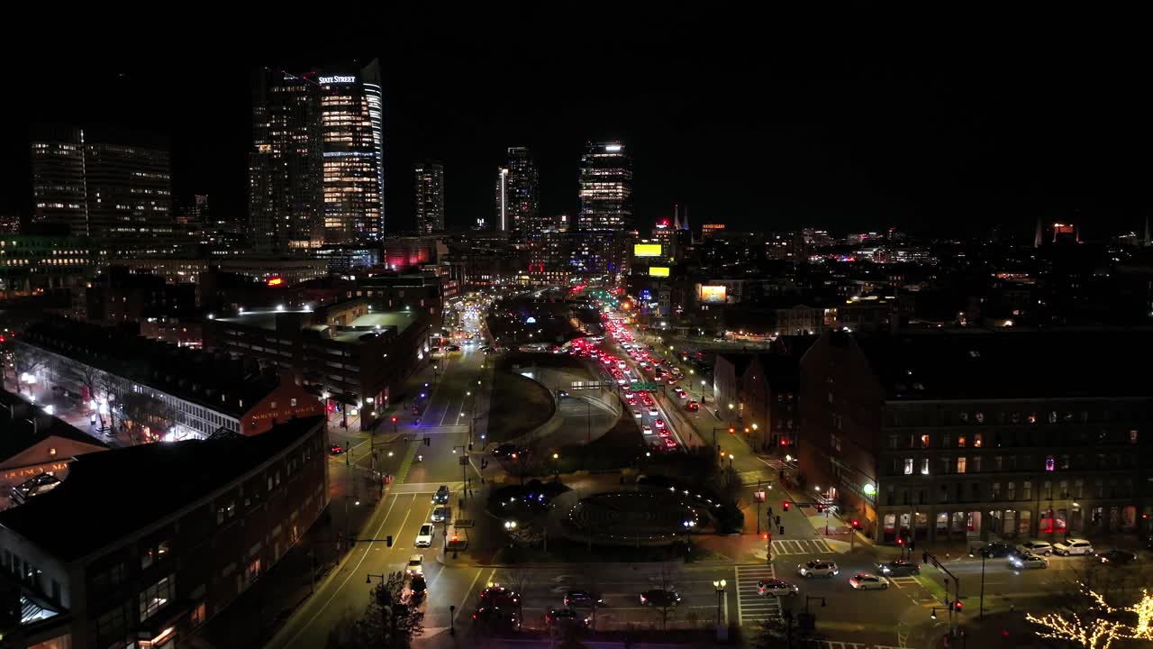 Nighttime cityscape along Boston’s Rose Kennedy Greenway. Faneuil Hall and Quincy Market glow beneath skyscrapers. Vibrant overhead vantage of traffic and lights, aerial.