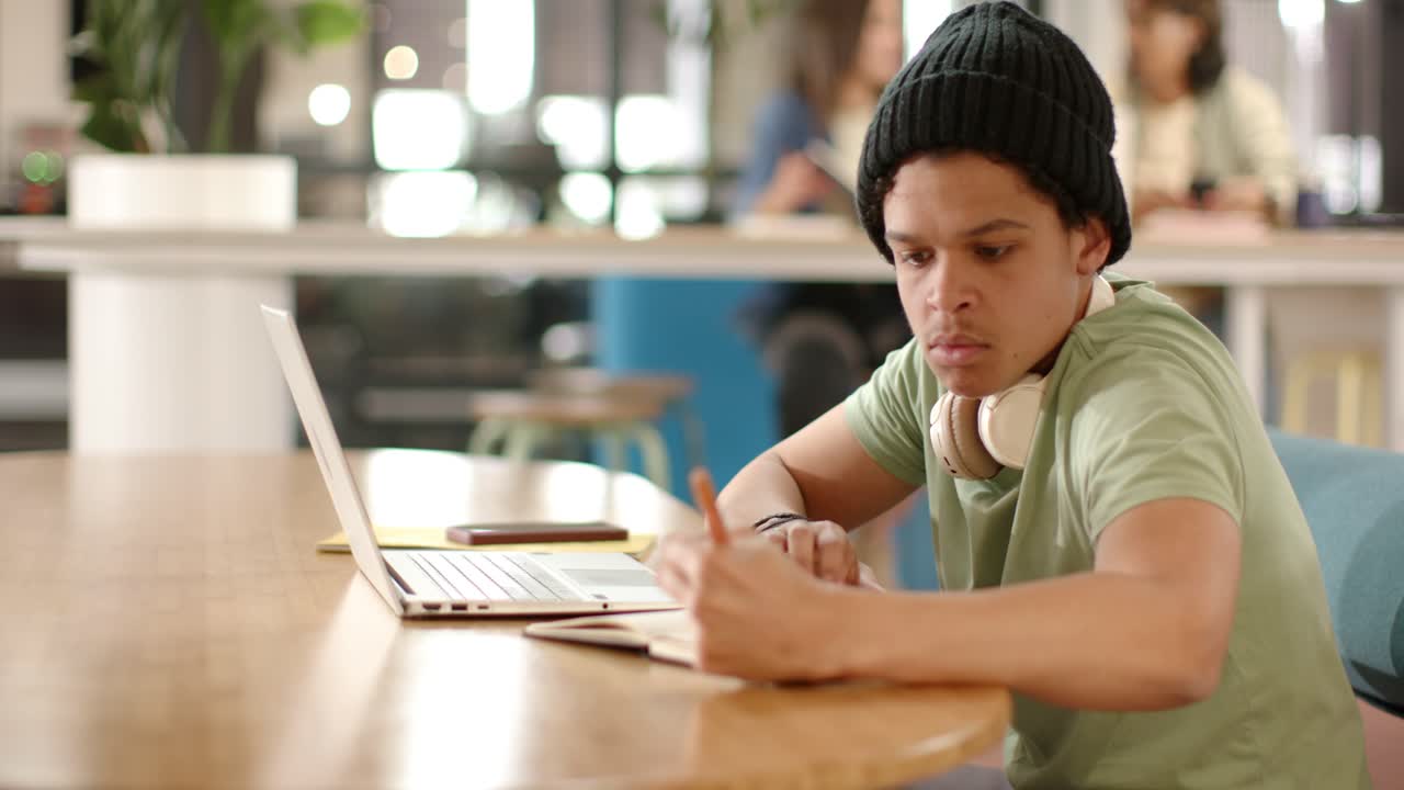 African American man studying, typing on laptop and writing in notebook at shared table, copy space