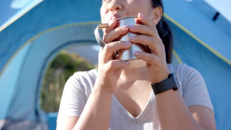 drinking from metal cup, woman enjoying outdoor camping experience in mountains