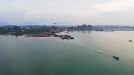 Long-tail-boat-sailing-away-from-jetty-on-misty-sea-coast-of-Thailand