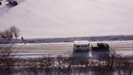 truck towing white horse trailer on rural road in winter season, aerial drone shot