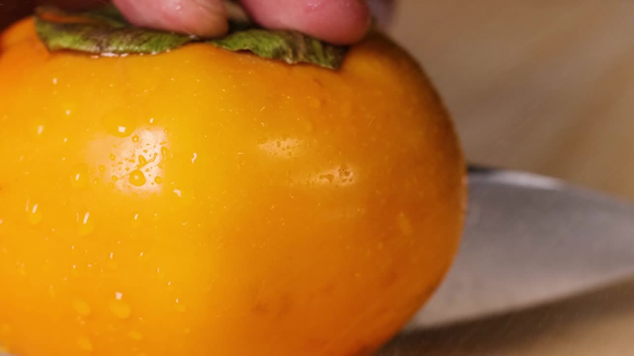 A detailed view of a knife slicing through a ripe persimmon, highlighting the fruit's texture and color.