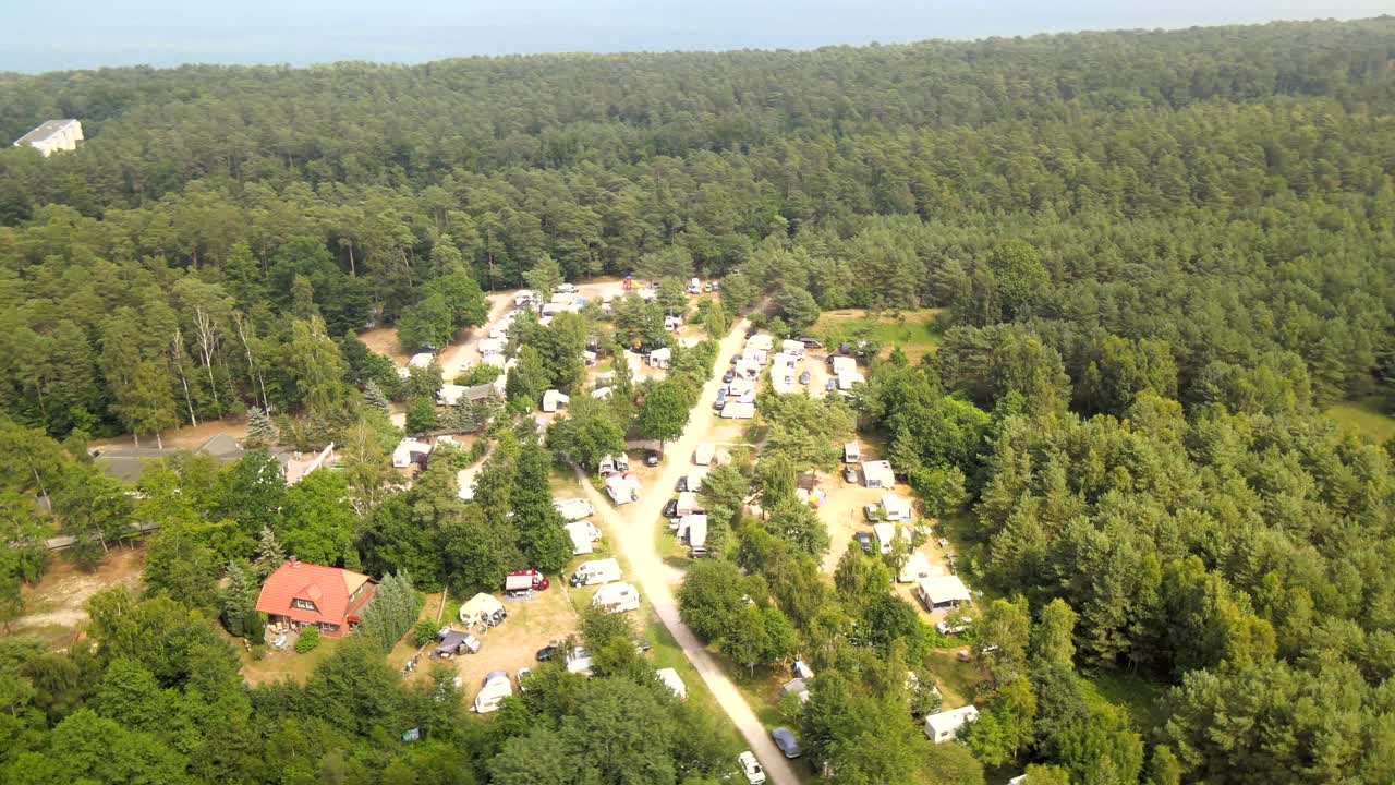 Drone shot of a coastal campsite on Rügen, nestled in lush forest near the Baltic Sea, filled with tents and caravans.
