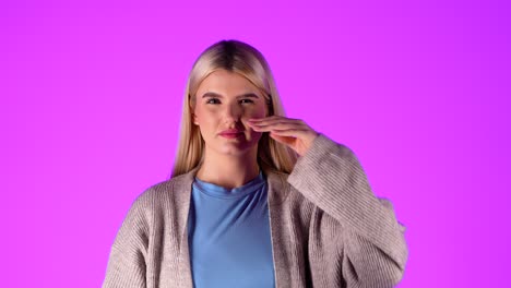 mujer seria se frota la nariz con la mano sufriendo de frío, fotografía de estudio, retrato con fondo infinito violeta