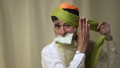 Fotografía-De-Estudio-De-Un-Hombre-Sikh-Mayor-Con-Barba-Atando-Una-Tela-Para-Un-Turbante-Contra-Un-Fondo-Liso,-Filmada-En-Tiempo-Real-2