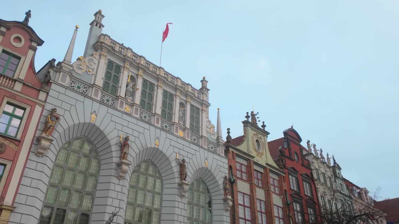 Vista dal basso dello storico Palazzo Artus e delle tradizionali case mercantili colorate a Danzica, Polonia. Ideale per documentari di viaggio e contenuti sul patrimonio europeo